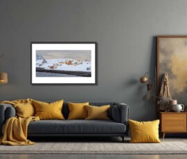 Fine-art photography print titled Arctic winter Sarnesfjorden I by Eva Eidsheim Photography. Showing a color cultural landscape of a tiny coastal settlement in Nordkapp on an icy winter day. Waves crash against the shore of a snow-covered landscape under a dark sky, capturing a raw Arctic atmosphere, printed on premium Hahnemühle art paper.