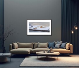 Fine-art photography print titled Arctic winter Sarnesfjorden I by Eva Eidsheim Photography. Showing a color cultural landscape of a tiny coastal settlement in Nordkapp on an icy winter day. Waves crash against the shore of a snow-covered landscape under a dark sky, capturing a raw Arctic atmosphere, printed on premium Hahnemühle art paper.