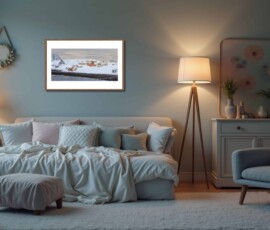 Fine-art photography print titled Arctic winter Sarnesfjorden I by Eva Eidsheim Photography. Showing a color cultural landscape of a tiny coastal settlement in Nordkapp on an icy winter day. Waves crash against the shore of a snow-covered landscape under a dark sky, capturing a raw Arctic atmosphere, printed on premium Hahnemühle art paper.